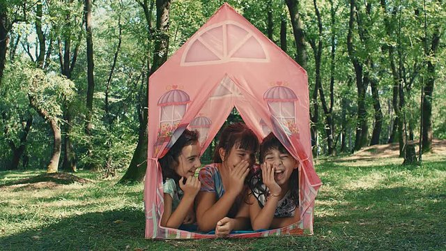 Three girlfriends playing gossiping lying in tent toy in the park, 4k