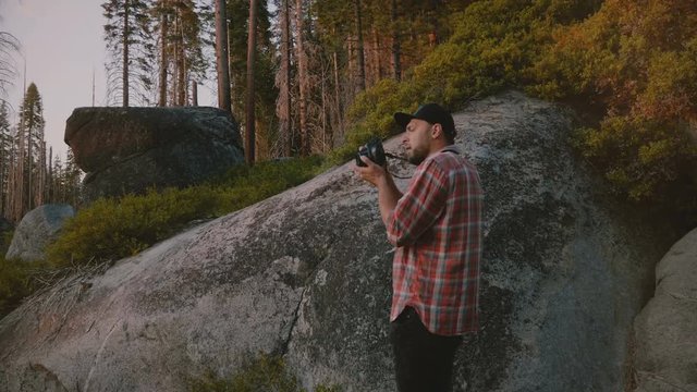 Back view young male photographer standing at a rock taking photos at beautiful sunset Yosemite park forest slow motion.
