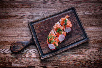 A wooden tabletop on which lies a board of sandwiches with salmon greens.