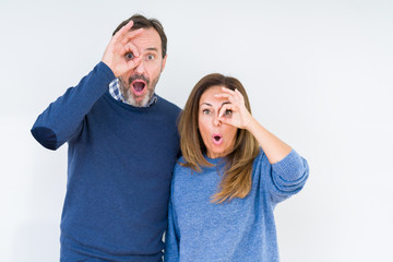 Fototapeta premium Beautiful middle age couple in love over isolated background doing ok gesture shocked with surprised face, eye looking through fingers. Unbelieving expression.
