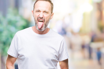 Middle age hoary senior man wearing white t-shirt over isolated background sticking tongue out happy with funny expression. Emotion concept.