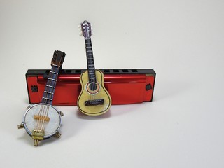 A miniature banjo and a miniature acoustic guitar propped up on a red 10-hole diatonic harmonica