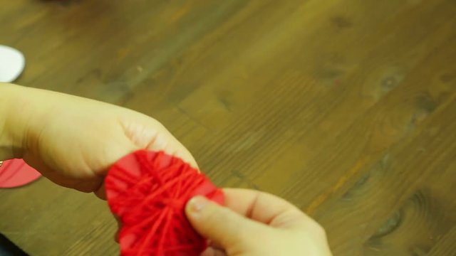 The girl makes a suverner from a red heart of cardboard and thread. Time laps.
