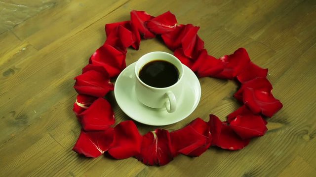 The girl puts in the middle of the heart of rose petals a cup of coffee.