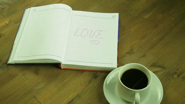 The girl writes the word love in the diary and drinks coffee. Time laps