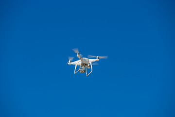 Drone in flight, green trees in the background, selective focus on the drone.