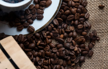 Closeup coffee beans coming out of a wooden barrel next to a white coffee cup