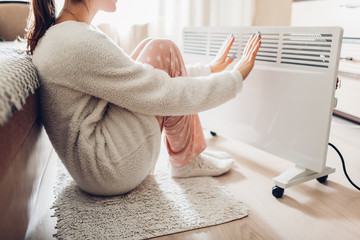 Using heater at home in winter. Woman warming her hands. Heating season.
