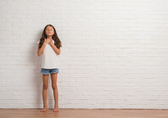 Young hispanic kid stading over white brick wall smiling with hands on chest with closed eyes and grateful gesture on face. Health concept.
