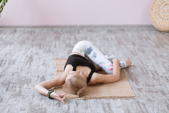 Fitness woman practices yoga asana Jathara Parivartanasana, twisting posture