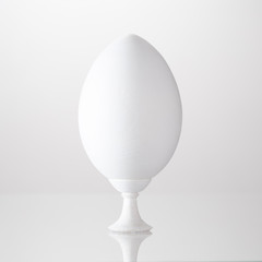 Decorative wooden egg on a stand primed with white paint.