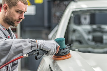 Employee in the shop painting the car body polishes painted body parts