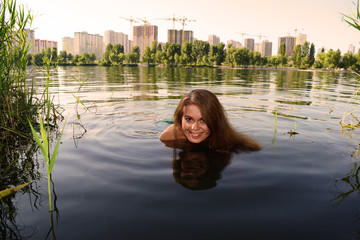 Portrait of a young cheerful fat girl in the water on the lake near the city.