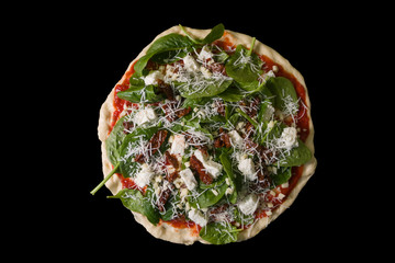 Raw uncooked pizza with spinache dried tomatoes and feta cheese on black background.