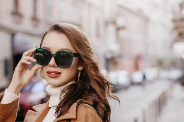 Outdoor close up portrait of young beautiful woman wearing big stylish green sunglasse, model walking in street. Copy, empty space for text