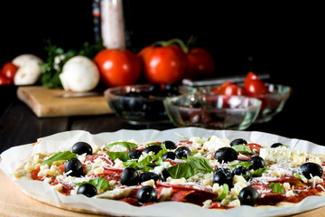 Raw uncooked pizza with pepperoni salami, black olives, basil and cheese.