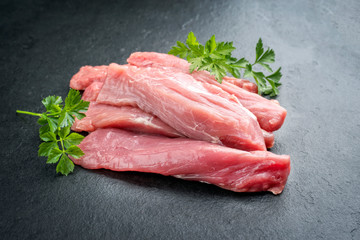 Rohe Spanferkel Filet mit Kräutern angeboten als closeup auf einem schwarzen Board  