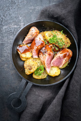 Fried suckling pig fillet with potatoes and hot sauce offered as top view in a modern design cast- iron pan with herbs