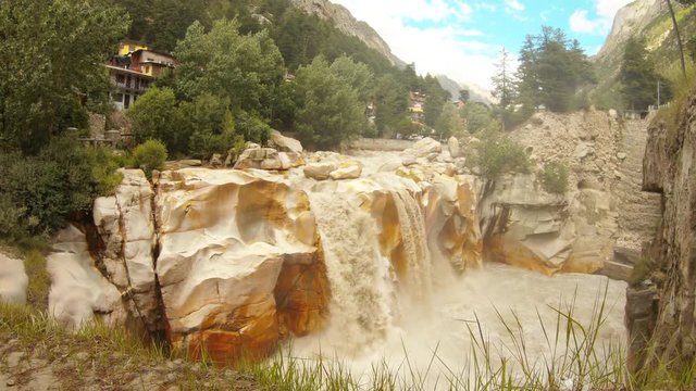 Waterfall Surya Kund on holy river Ganges on background mountain town Gangotri deodars blue sky with white clouds