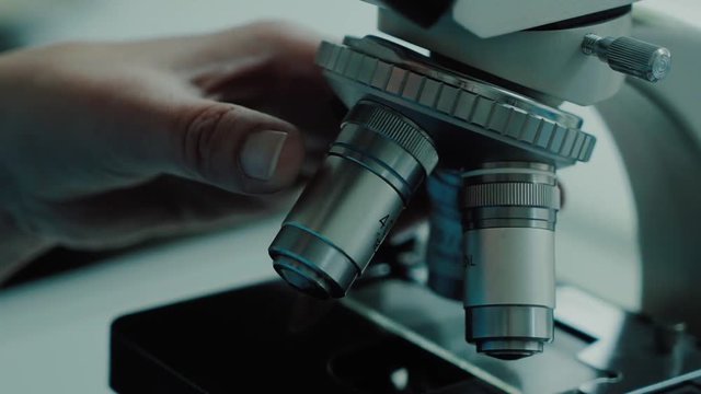 Male hands are rotating lenses of medical microscope in a laboratory. He is regulating gadget for exploring a samples, close-up