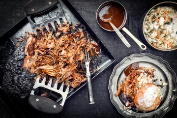  Traditioneel barbecue pulled pork stuk Bosten aan stukken gescheurd met coleslaw en burger als bovenaanzicht op een plank © HLPhoto