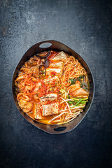 Traditional Korean kimchi jjigae with grilled pork belly and ramen as closeup in a modern design Japanese cast-iron roasting dish
