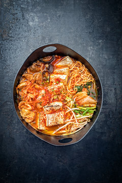Traditional Korean kimchi jjigae with grilled pork belly and ramen as closeup in a modern design Japanese cast-iron roasting dish