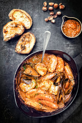 Traditional Catalan fish stew romesco de peix with prawns, mussels and fish as top view in a modern design cast-iron roasting dish