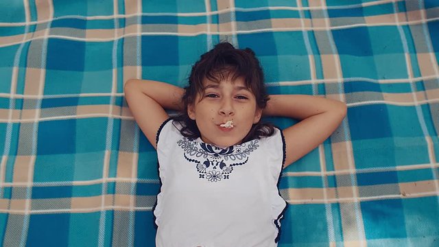 Top view of a little girl lying on picknick blanket blowing bubblegum candy bubbles, slow motion, 4k