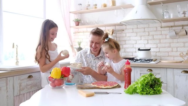 Father and daughters having a fun in the kitchen and making pizza