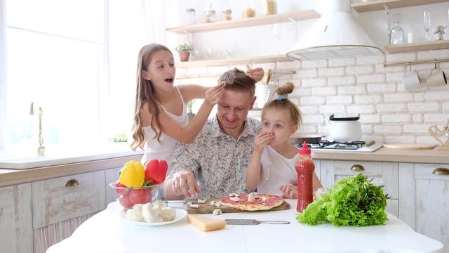 Father and daughters having a fun in the kitchen and making pizza