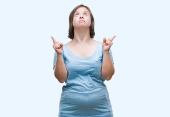 Fototapeta premium Young adult woman with down syndrome over isolated background amazed and surprised looking up and pointing with fingers and raised arms.