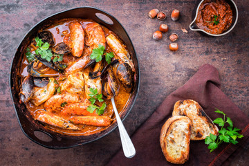 Traditional Catalan fish stew romesco de peix with prawns, mussels and fish as top view in a modern...