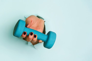 Woman hand holding blue dumbbell on blue background. Fitness, sport, healthy lifestyle, diet...