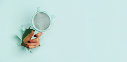 Female hand holding sieve flour through hole on blue background. Backing and cooking concept. Banner with copy space