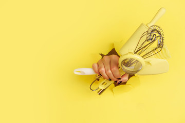 Woman hand holding kitchen utensils on yellow background. Baking tools - brush, whisk, spatula. Bakery, cooking, healthy homemade food concept. Copy space