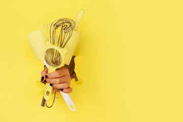 Woman hand holding kitchen utensils on yellow background. Baking tools - brush, whisk, spatula. Bakery, cooking, healthy homemade food concept. Copy space