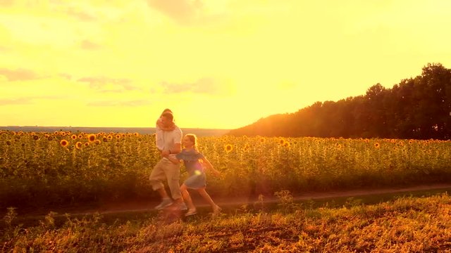 Father holding daughters by hands running near sunflower evening field