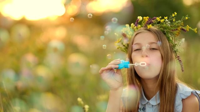 Girl is blowing bubbles on the meadow and during sunset