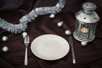 empty plate on dark linen witch christmas balls and lantern