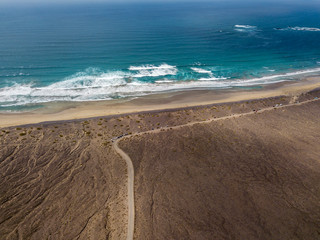Vista aerea della spiaggia di Famara, Lanzarote, isole Canarie, Spagna. Risco di Famara, rilievo, montagne a picco sull’Oceano Atlantico. Strada non asfaltata che costeggia la costa
