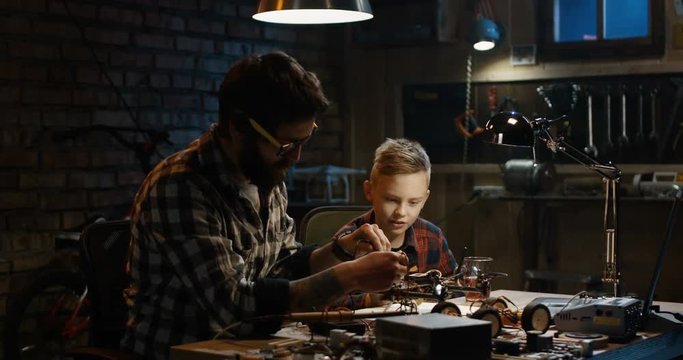 Medium shot of a father and son repairing a drone with wireless control in a garage