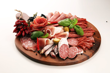 Food tray with delicious salami, pieces of sliced prosciutto crudo, sausage and basil. Meat platter with selection