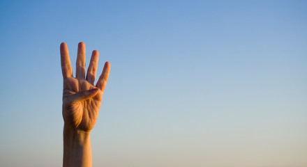 Hand doing / showing number four gesture symbol on blue summer sky nature background. Gesturing number 4. Number four in sign language. Fourth and counting down four concept. Four fingers up.