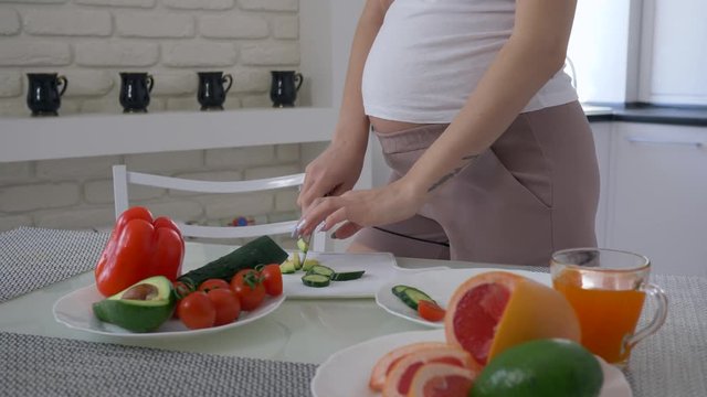 natural food for pregnancy, maternity girl with big abdomen is cooking useful salad for healthy tasty lunch from fresh vegetables at cuisine