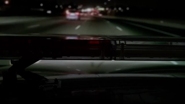 POV Police highway patrol car with red blue flash emergency lights driving on freeway at night.