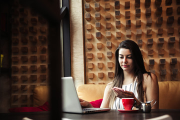 Young pretty caucasian woman in cafe in city centre with tablet laptop