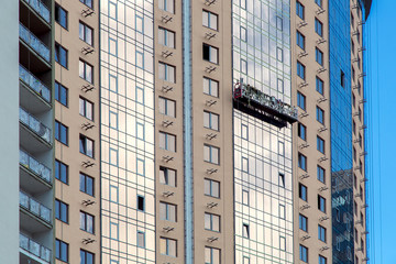 Construction cradle on the facade of a multi-storey building under construction performs glass works.