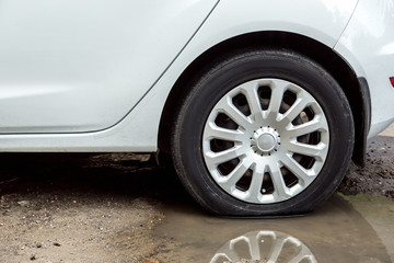 A dirty white car is standing in a puddle of water, a close-up of a wheel with a reflection of a wheel in a puddle.