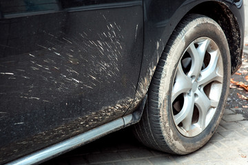 Close-up of a front wheel of a dirty car with a fender and a door dirtied with splashes of dirt.